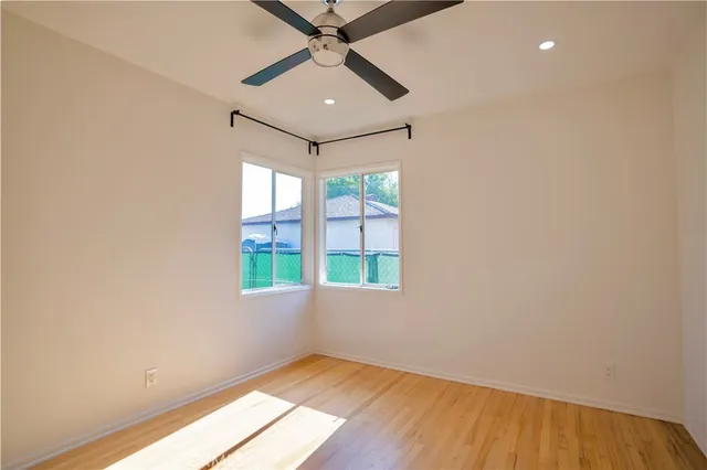 an empty room with wooden floor chandelier fan and windows