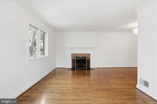 a view of an empty room with wooden floor fireplace and a window