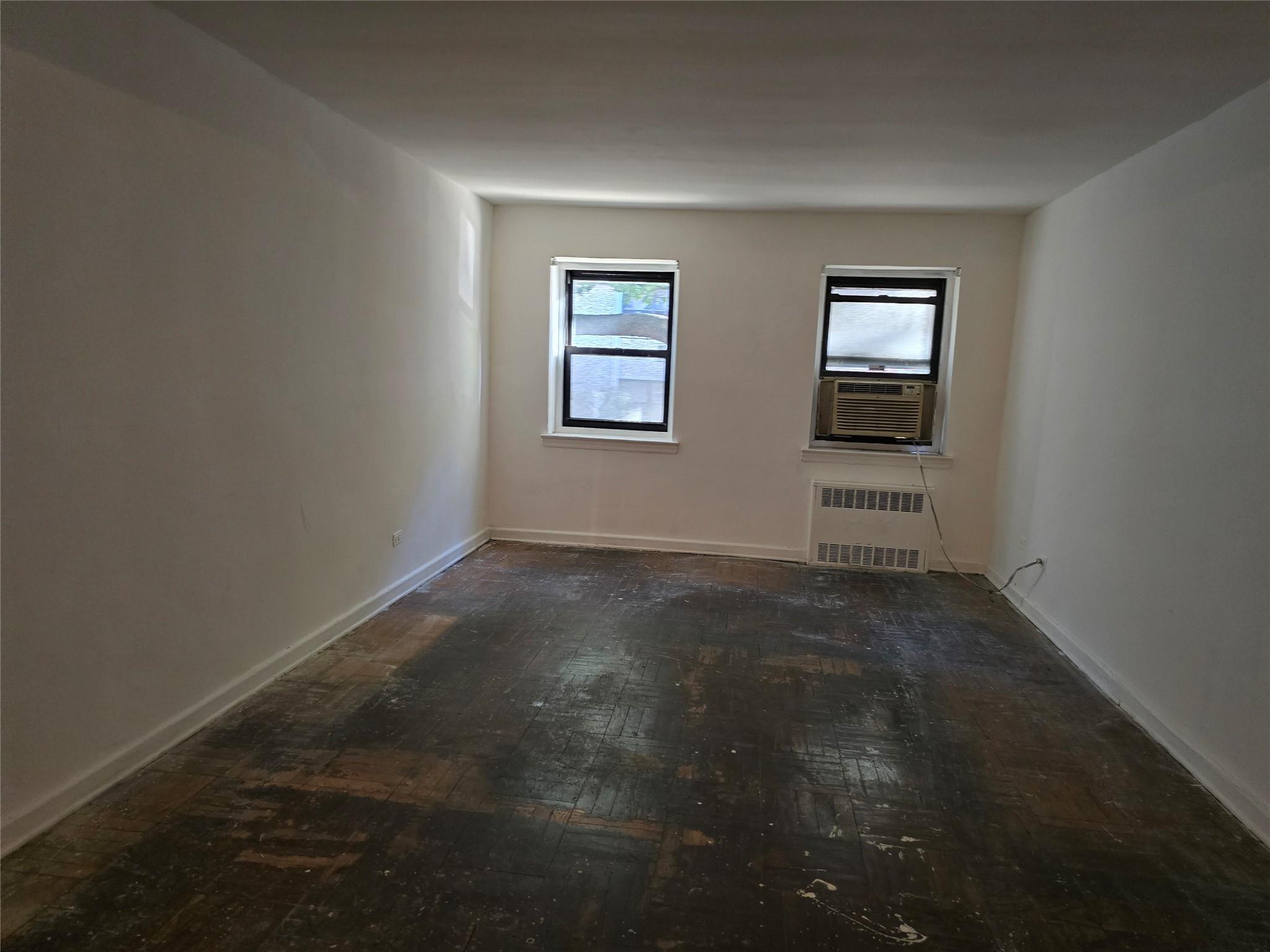 102-25 67th Road, Unit 1F Queens, NY 11375 - Photo 3 of 6 Empty room with cooling unit, dark parquet flooring, and radiator heating unit