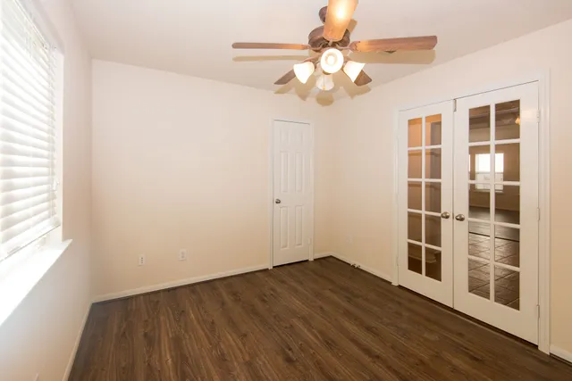 an empty room with wooden floor chandelier fan and windows