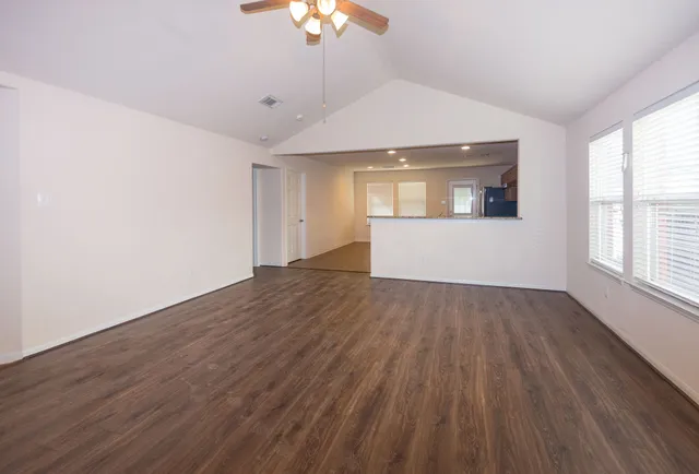 an empty room with wooden floor chandelier fan and windows