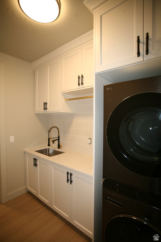 635 East Mountain Road North Ogden, UT 84414 - Photo 8 of 33 Laundry room featuring white shaker-style cabinetry with matte black hardware, a stainless steel sink with a matte black pull-down faucet, light-toned wood-finish flooring, and a stacked washer and dryer unit
