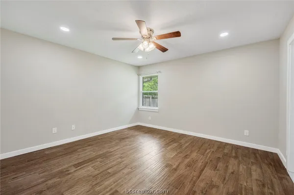 a view of an empty room with wooden floor and a ceiling fan