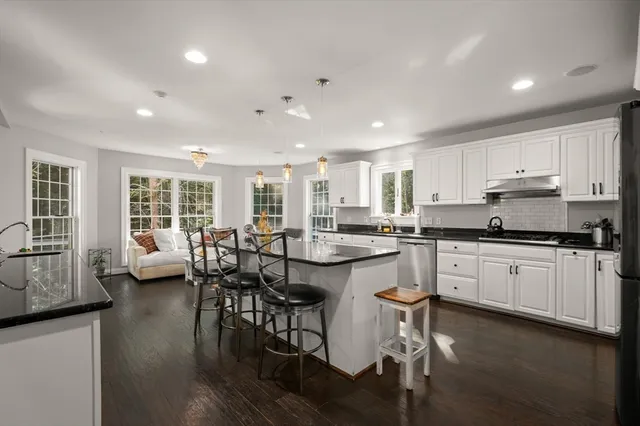 a kitchen with stainless steel appliances granite countertop a stove top oven a sink dishwasher a dining table and chairs with wooden floor