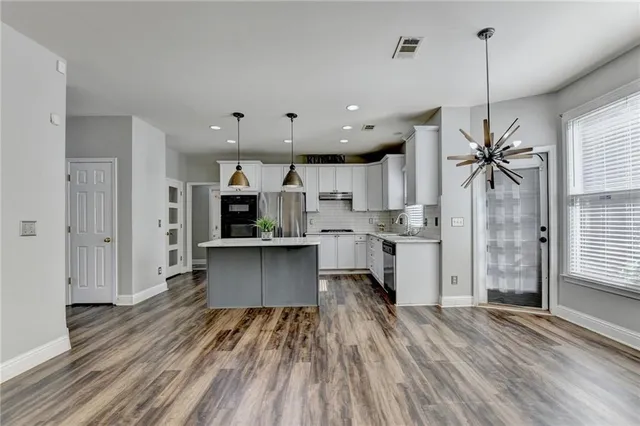 a kitchen with stainless steel appliances granite countertop a refrigerator a sink dishwasher a stove and white countertops with wooden floor