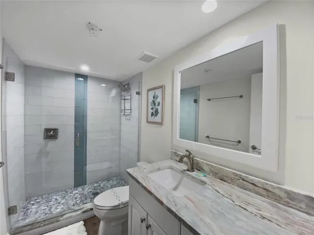 a bathroom with a granite countertop sink a toilet a mirror and shower
