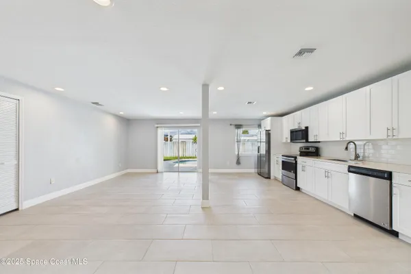 a living room with stainless steel appliances furniture a rug and a kitchen view
