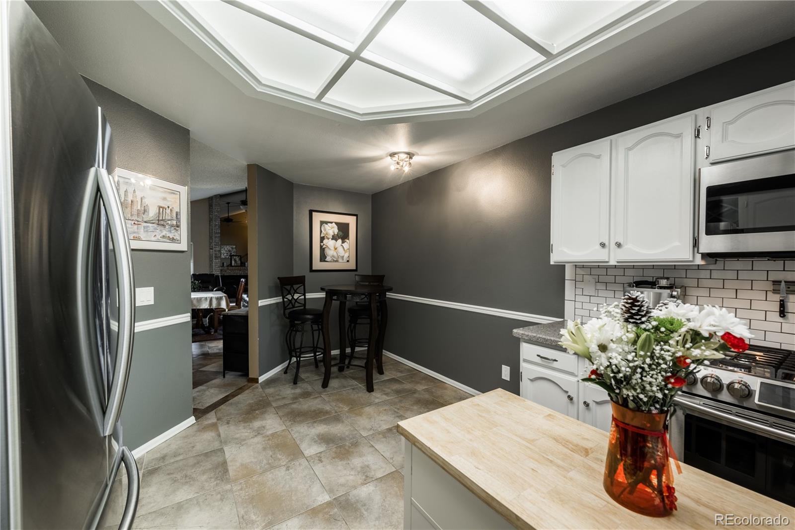 8583 Redstone Street Highlands Ranch, CO 80126 - Photo 5 of 25 a kitchen with stainless steel appliances kitchen island granite countertop a refrigerator a stove a sink dishwasher and white cabinets with wooden floor