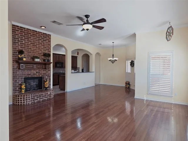 an empty room with wooden floor a ceiling fan a fireplace and windows