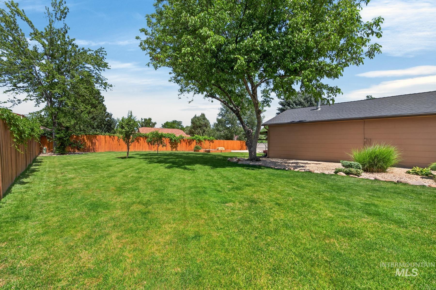 9622 Delaware Street Boise, ID 83709 - Photo 37 of 48 Expansive green lawn with a perimeter wood fence, mature shade trees, and landscaped rock beds