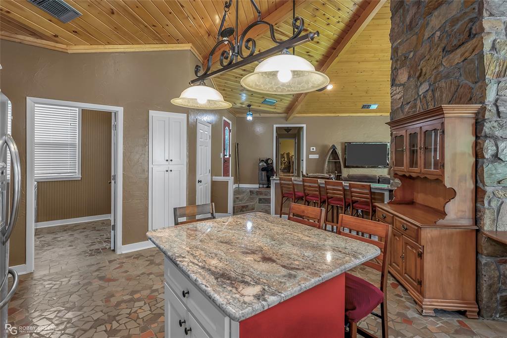 10865 Ferry Lake Road Oil City, LA 71061 - Photo 12 of 36 Kitchen with a wood ceiling with exposed beams, light stone finish floors, a kitchen breakfast bar, ornamental molding, and light stone countertops