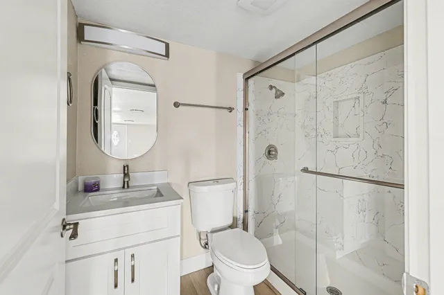 a bathroom with a toilet sink vanity granite and shower