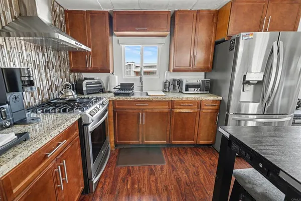 a kitchen with stainless steel appliances granite countertop a refrigerator a sink dishwasher a stove and white countertops with wooden floor