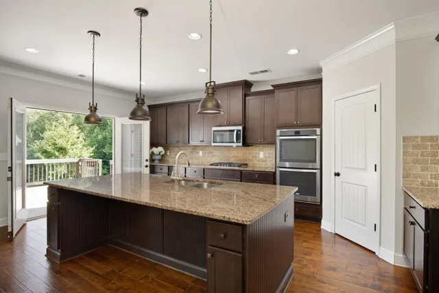 a kitchen with stainless steel appliances granite countertop wooden floors wooden cabinets a window and a sink