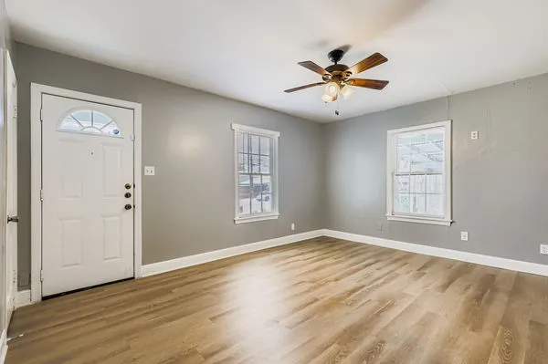 an empty room with wooden floor a ceiling fan and windows