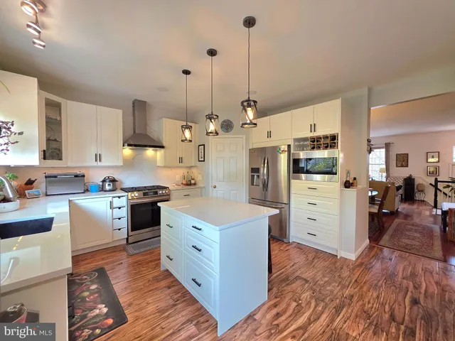 a kitchen with stainless steel appliances kitchen island granite countertop a sink a stove and a wooden floors