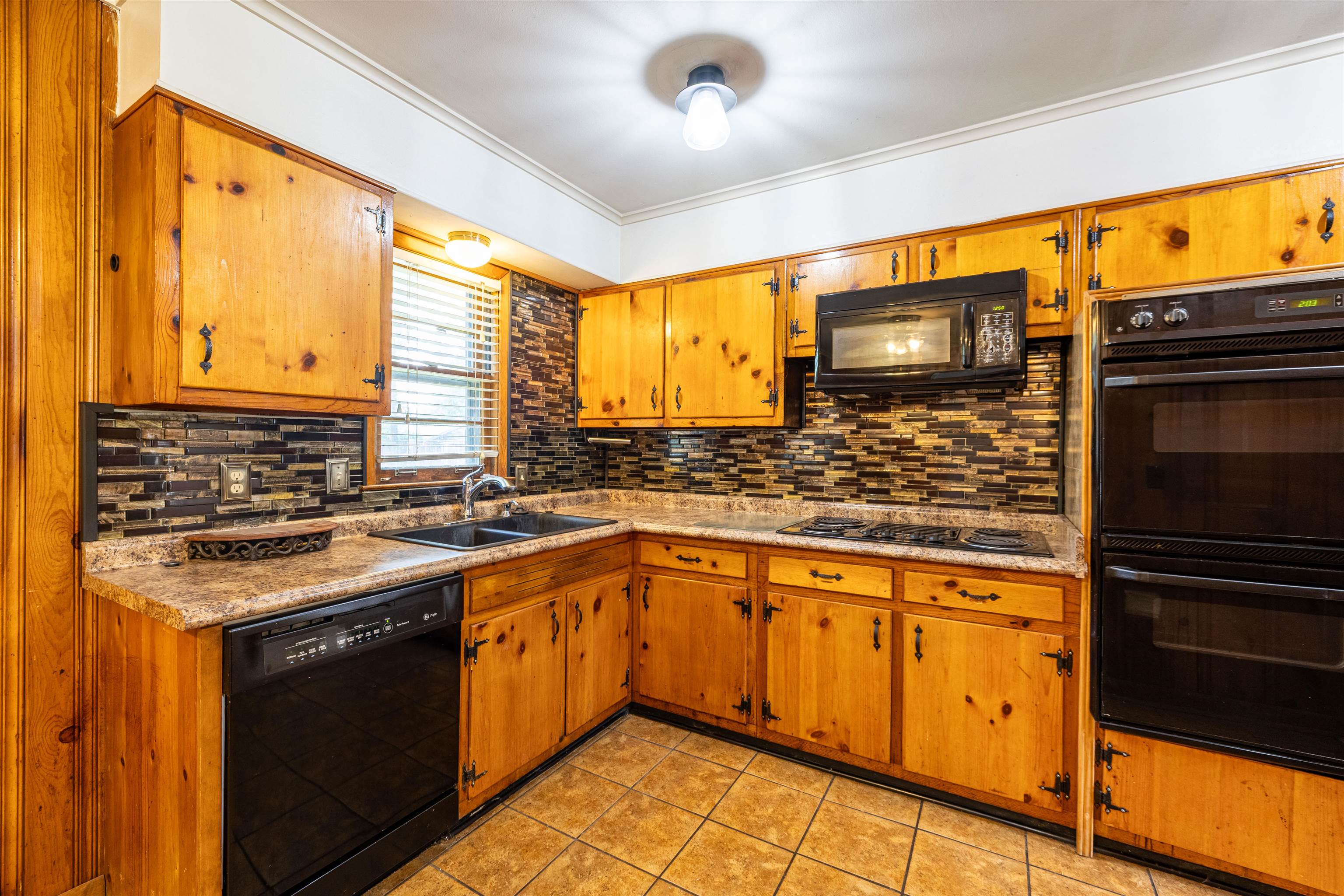 3953 Comanche Road Memphis, TN 38118 - Photo 12 of 24 Kitchen featuring black appliances, backsplash, light tile patterned flooring, brown cabinetry, and crown molding
