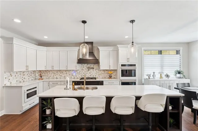 a kitchen with stainless steel appliances kitchen island granite countertop a dining table chairs and white cabinets