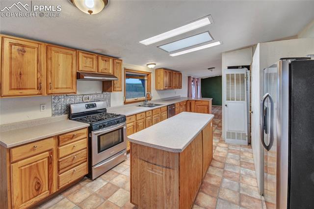 7940 Edison Road Yoder, CO 80864 - Photo 15 of 38 Kitchen with appliances with stainless steel finishes, a center island, light countertops, a heating unit, and under cabinet range hood