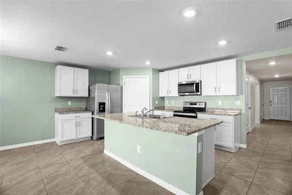 a kitchen with kitchen island granite countertop a stove top oven a sink dishwasher a refrigerator and white cabinets with wooden floor