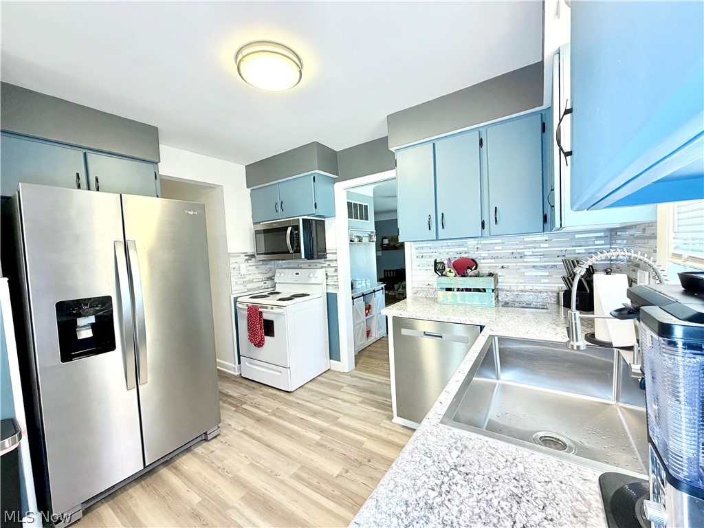 32125 Densmore Road Willowick, OH 44095 - Photo 8 of 23 Kitchen featuring light blue cabinetry with dark hardware, stainless steel appliances, granite countertops, and a mosaic tile backsplash