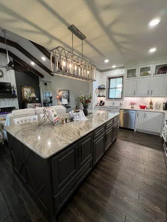 a kitchen with kitchen island granite countertop a sink stainless steel appliances wooden floor and chandelier