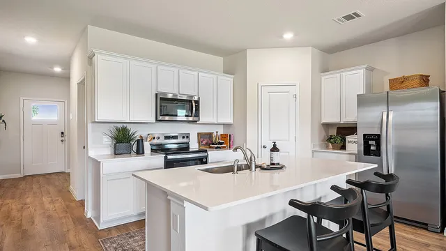 a kitchen with a refrigerator a stove a sink and white cabinets with wooden floor