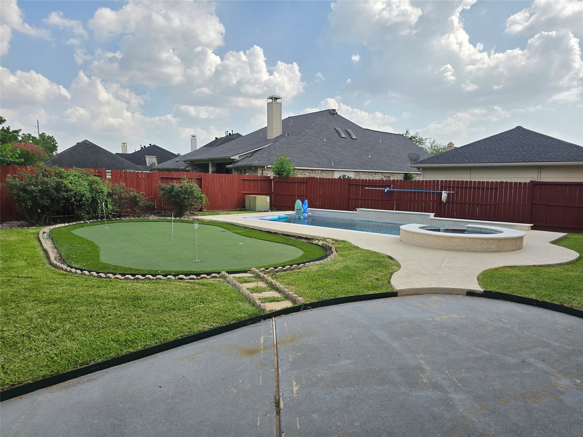 6506 Monte Bello Ridge Lane Houston, TX 77041 - Photo 17 of 39 This backyard features a spacious pool with an attached hot tub, a mini putting green, and a well-maintained lawn, all enclosed by a red wooden fence for privacy. Perfect for relaxation and outdoor entertainment.