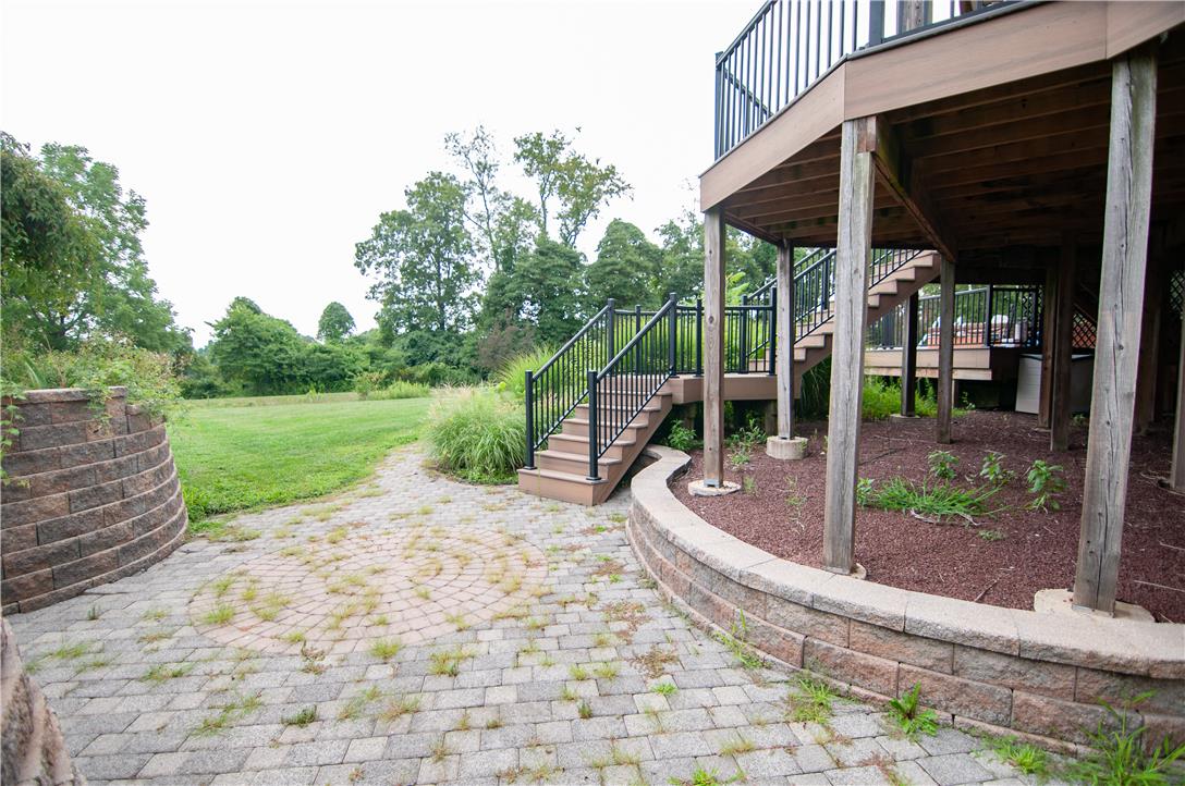 2202 High Meadow Road Coopersburg, PA 18036 - Photo 41 of 41 Multi-level decking and stone retaining walls frame a stone-paved patio overlooking a grassy backyard.