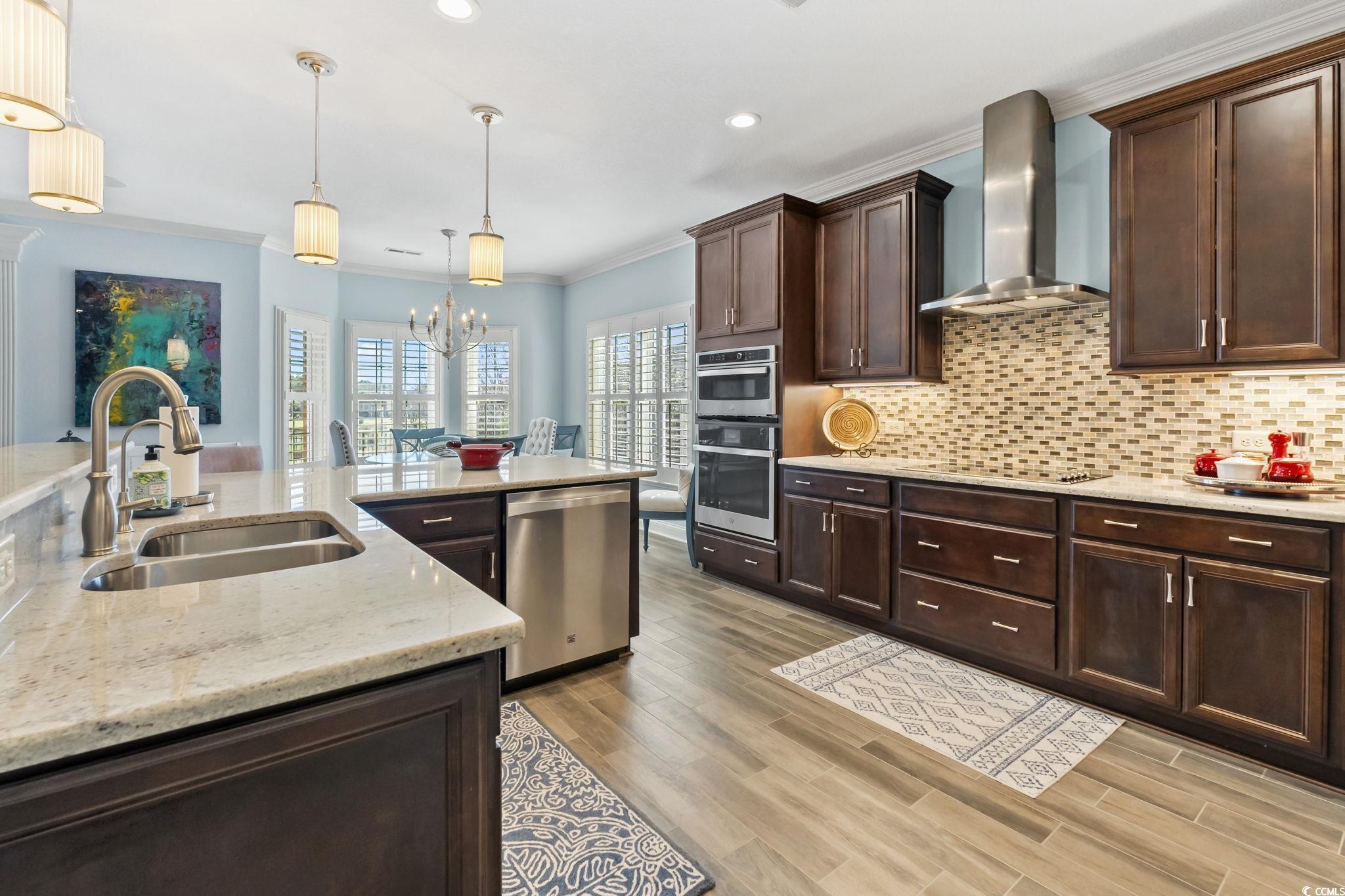 750 Villarosa Drive Myrtle Beach, SC 29572 - Photo 8 of 40 Kitchen with dark brown cabinets, crown molding, a chandelier, wall chimney range hood, and decorative light fixtures