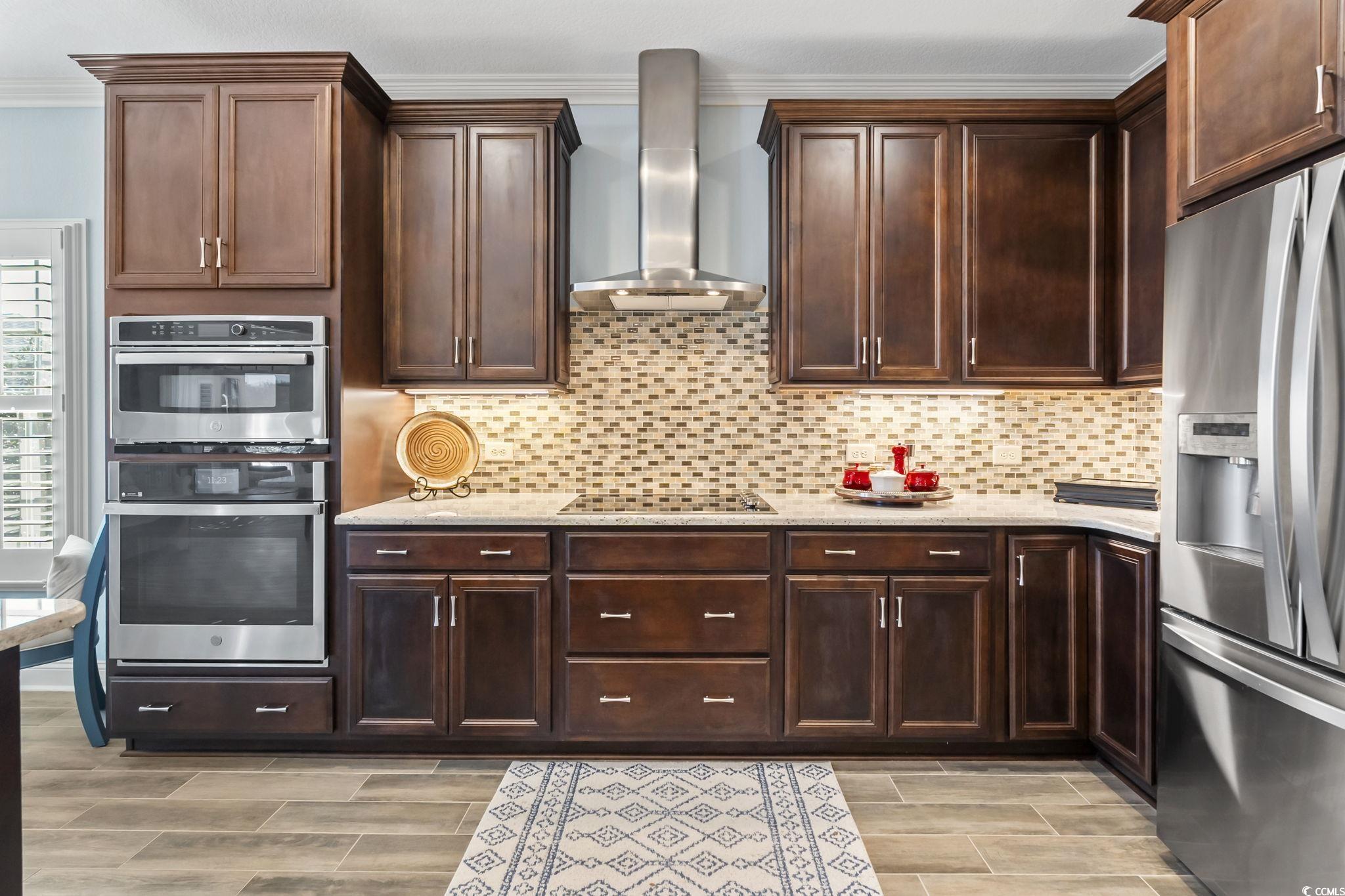 750 Villarosa Drive Myrtle Beach, SC 29572 - Photo 9 of 40 Kitchen featuring stainless steel appliances, wall chimney exhaust hood, crown molding, light stone countertops, and decorative backsplash