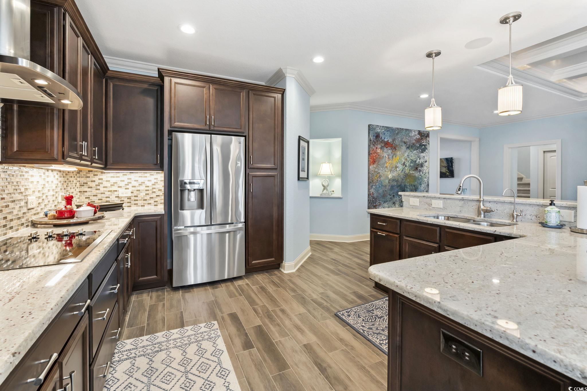 750 Villarosa Drive Myrtle Beach, SC 29572 - Photo 10 of 40 Kitchen with wall chimney exhaust hood, stainless steel fridge, dark brown cabinetry, light stone counters, and hanging light fixtures