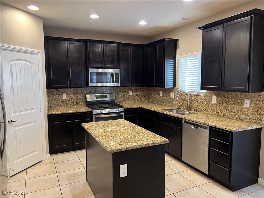 1070 Bobby Basin Avenue Henderson, NV 89014 - Photo 5 of 23 Kitchen featuring appliances with stainless steel finishes, tasteful backsplash, light tile patterned flooring, light stone counters, and dark cabinets