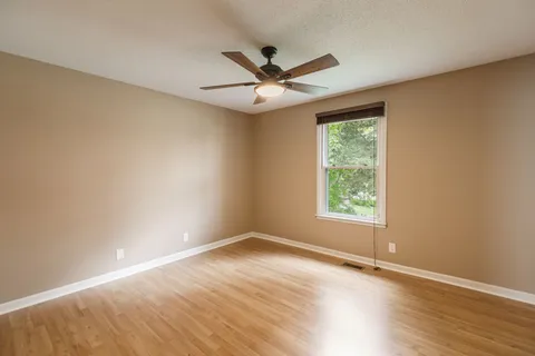 an empty room with wooden floor ceiling fan and windows