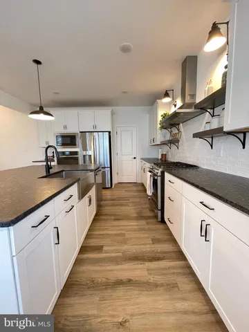 a view of a refrigerator in kitchen and an empty room with wooden floor