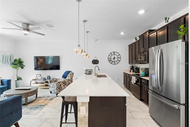 a kitchen with stainless steel appliances kitchen island granite countertop a refrigerator a stove a sink a dining table and chairs with wooden floor