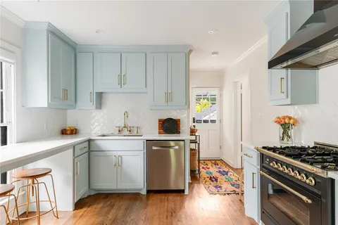 a kitchen with stainless steel appliances a stove a sink dishwasher and white cabinets with wooden floor