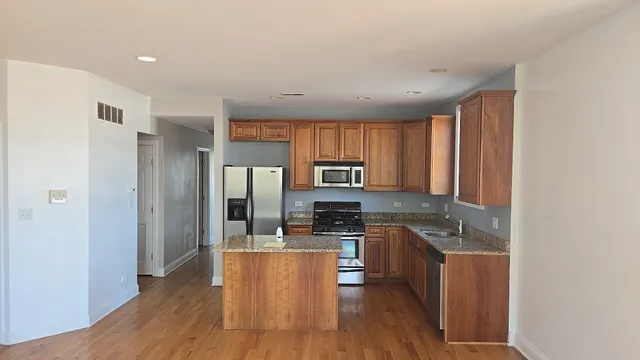 a kitchen with stainless steel appliances granite countertop a stove a sink a refrigerator white cabinets and wooden floor