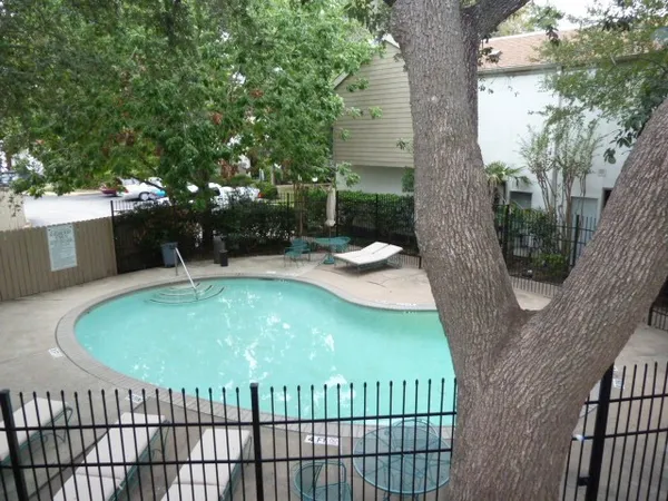 a view of swimming pool with lawn chairs and large trees