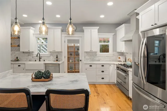 a kitchen with stainless steel appliances kitchen island granite countertop a sink a stove a refrigerator and white cabinets with wooden floor