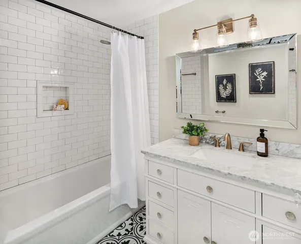 a bathroom with a granite countertop sink a mirror a bathtub and shower