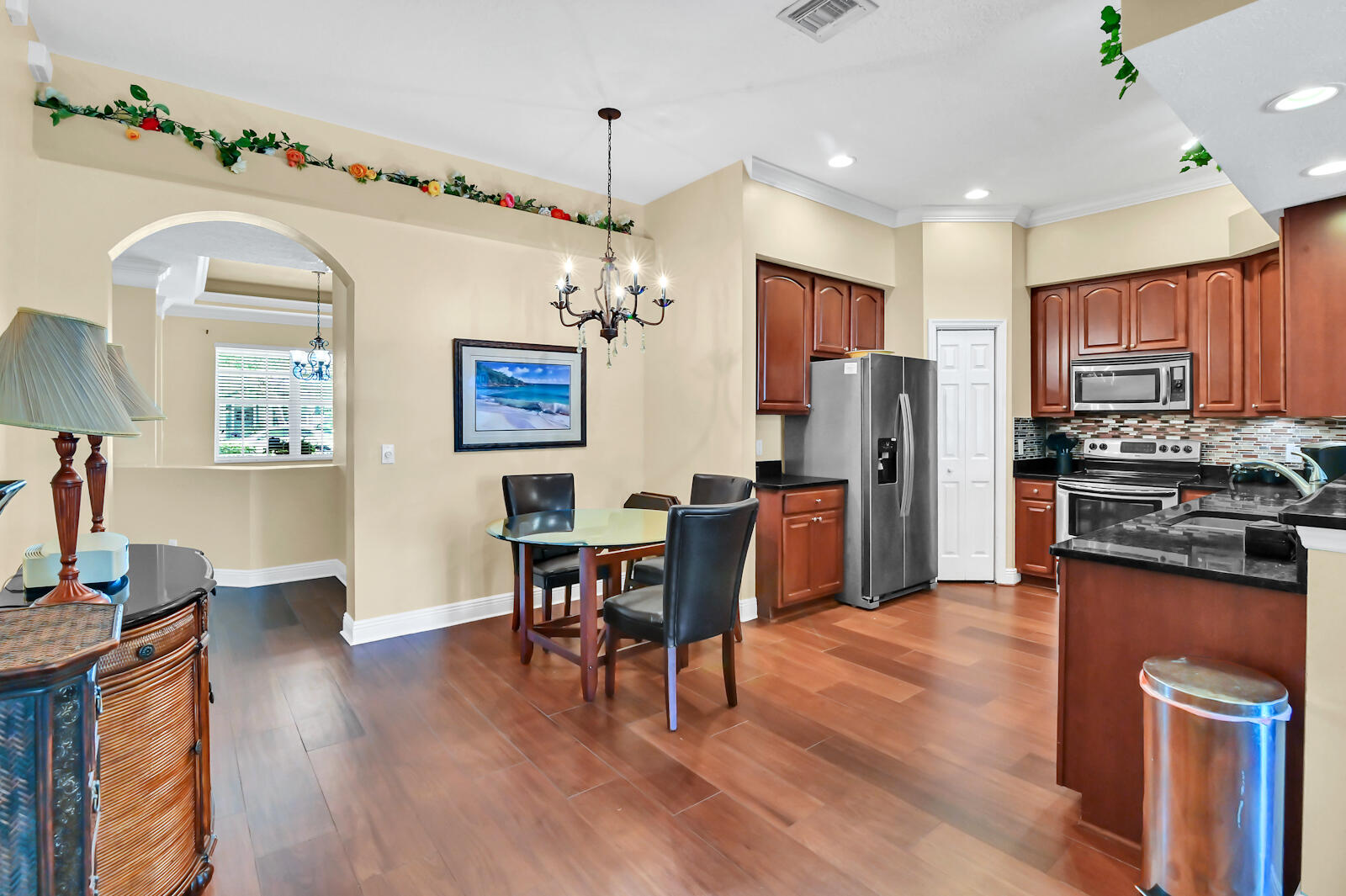 244 Clocktower Drive Jupiter, FL 33458 - Photo 11 of 36 a kitchen with stainless steel appliances granite countertop a refrigerator a stove top oven a dining table and chairs with wooden floor