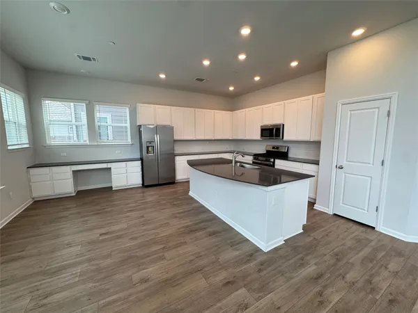 a large kitchen with stainless steel appliances granite countertop a stove a sink a refrigerator and white cabinets with wooden floor