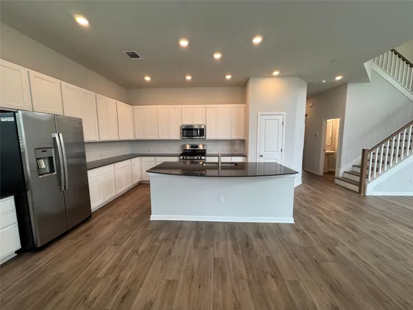 a kitchen with stainless steel appliances granite countertop a refrigerator a sink dishwasher a stove and white countertops with wooden floor