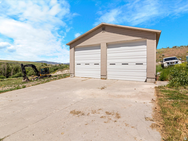 15680 North Beaver Dam Road Collinston, UT 84306 - Photo 42 of 49 Two-car garage featuring tan horizontal siding, white panel garage doors, and a concrete driveway