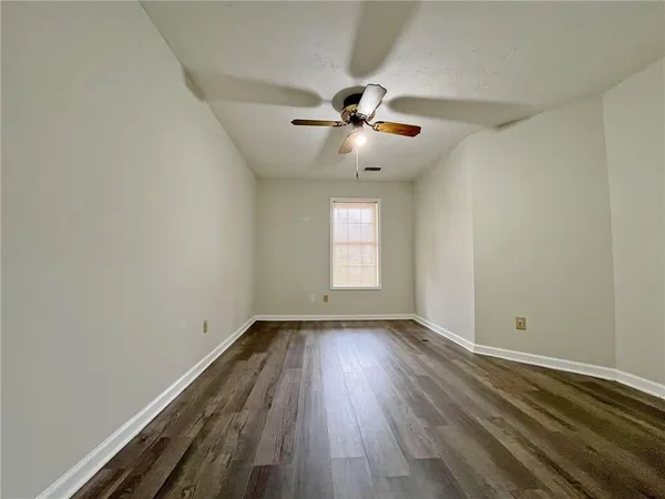 an empty room with wooden floor chandelier fan and windows
