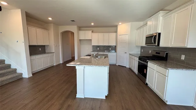 a kitchen with stainless steel appliances kitchen island granite countertop a stove a sink a refrigerator and white cabinets with wooden floor