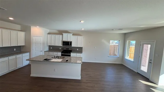 a kitchen with stainless steel appliances a stove a sink a refrigerator white cabinets and a wooden floor