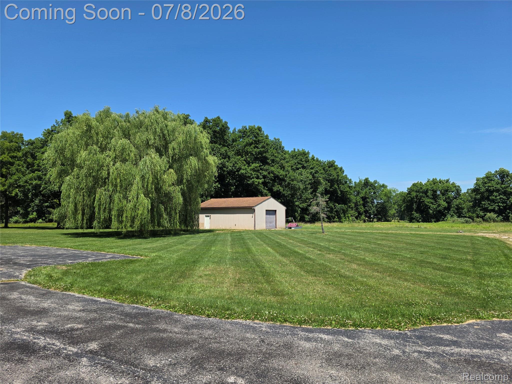 3581 North Burkhart Road Howell, MI 48855 - Photo 4 of 15 Expansive green lawn with visible mow lines, featuring a mature weeping willow tree and a light-colored outbuilding with a brown roof