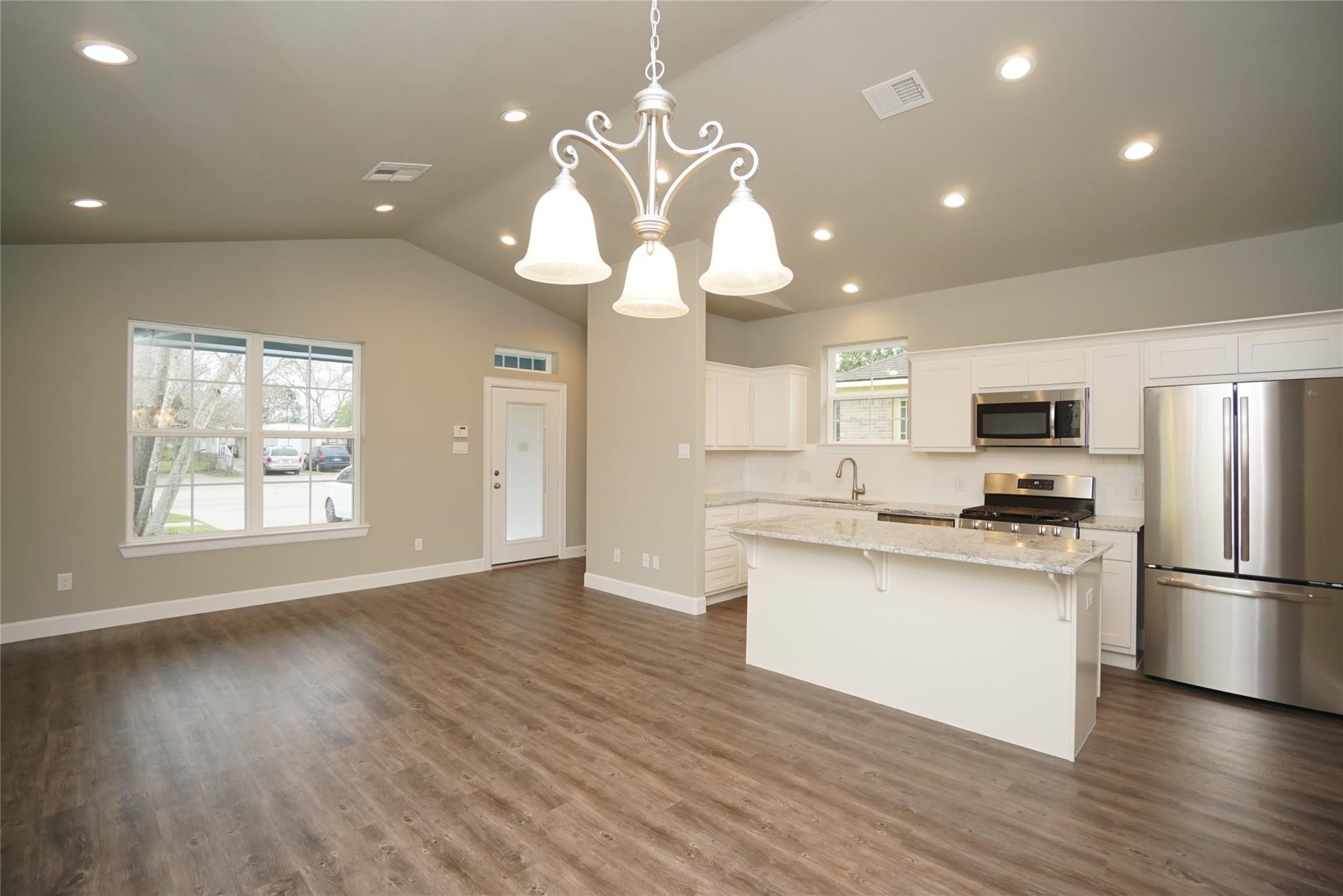 a kitchen with stainless steel appliances granite countertop a refrigerator a sink dishwasher a oven and a dining table with wooden floor